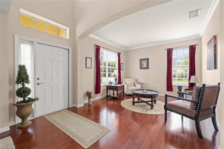 Foyer featuring arched walkways, dark wood-style floors, ornamental molding, and windows