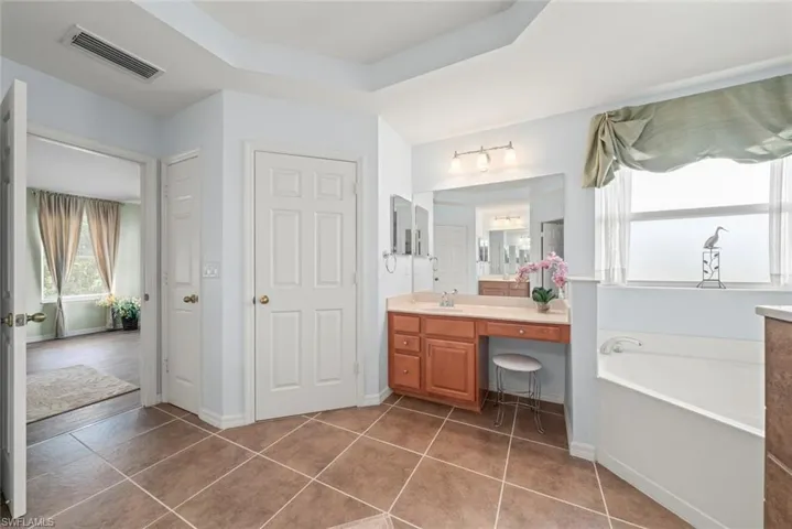 Primary bath featuring tile patterned flooring, a bath tub, vanity, and walk in closet door