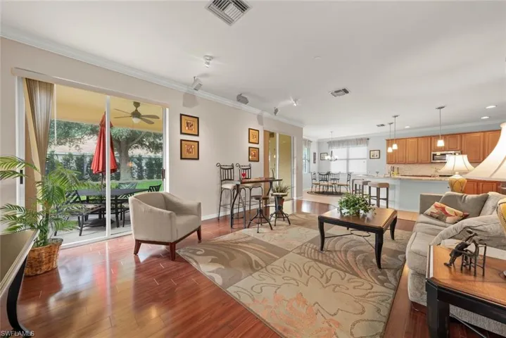Family room with laminate flooring, healthy amount of natural light with two sliding glass doors with access to the lanai, ornamental molding, and a ceiling fan
