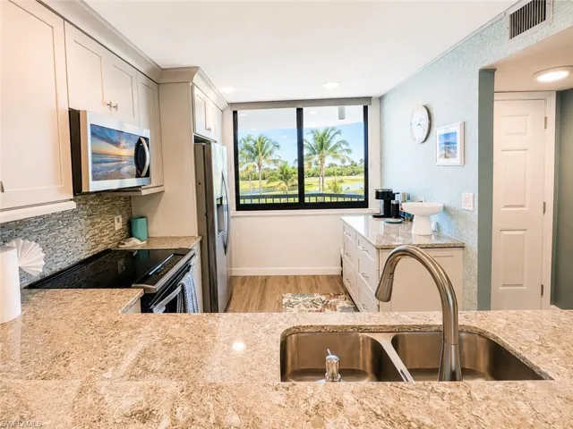 Kitchen featuring stone countertops, stainless steel appliances, white cabinetry, and a window with a tropical landscape beyond