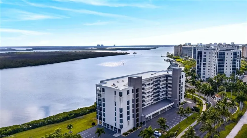 Waterfront condominium building featuring multiple balconies, covered parking, and landscaping with palm trees