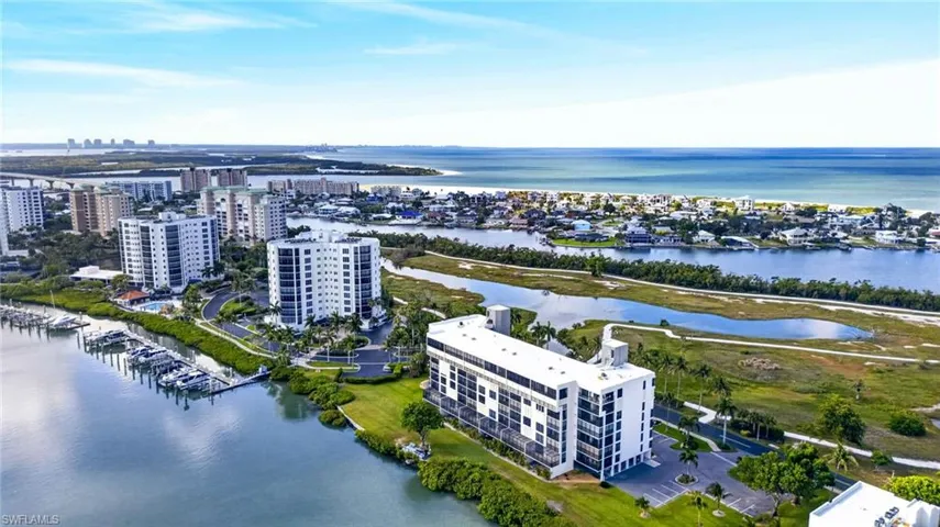 Expansive coastal aerial showcasing multiple waterfront high-rises, a marina with docked boats, and a distant beachfront