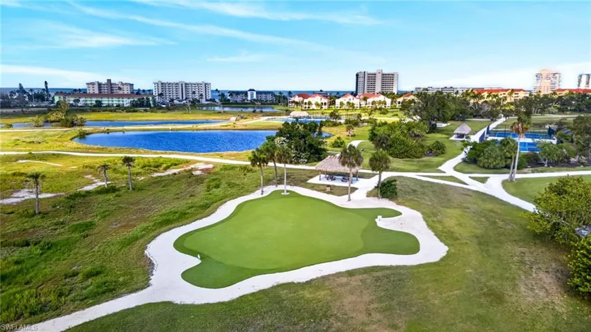 Putting green with sand trap, surrounded by green spaces, paved pathways, and mature palm trees