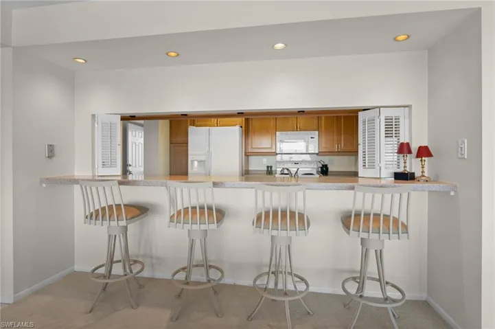 Kitchen featuring brown cabinets, a peninsula, white appliances, recessed lighting, and a breakfast bar area