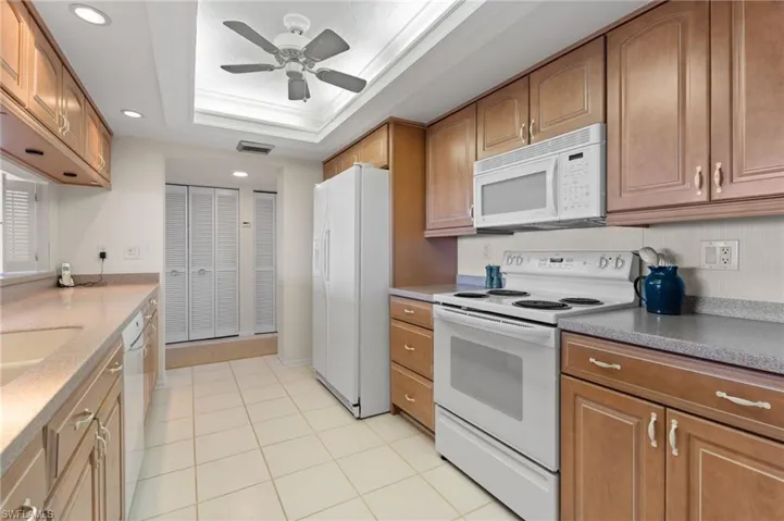 Kitchen featuring white appliances, a tray ceiling, ornamental molding, recessed lighting, and brown cabinetry
