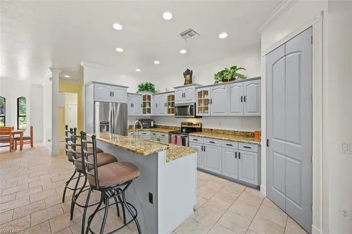 Kitchen featuring stainless steel appliances, ornamental molding, a kitchen bar, recessed lighting, and light stone counters