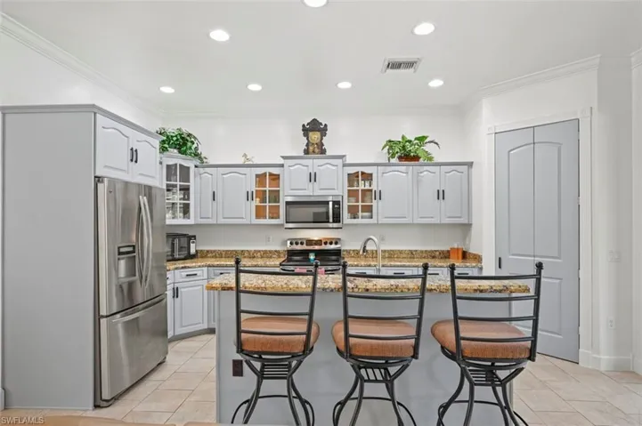 Kitchen with stainless steel appliances, light tile patterned floors, glass insert cabinets, a breakfast bar, and crown molding