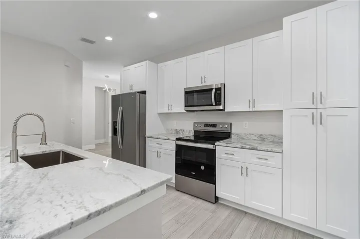Kitchen featuring appliances with stainless steel finishes, light stone counters, white cabinets, light wood-style flooring, and recessed lighting