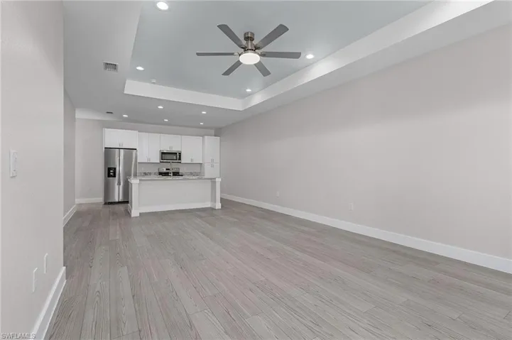 Unfurnished living room featuring recessed lighting, light wood finished floors, a ceiling fan, and a tray ceiling