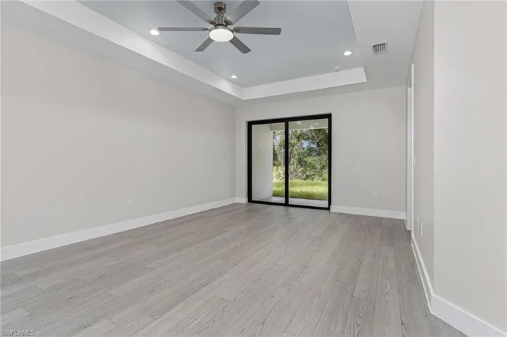 Spare room with a tray ceiling, light wood-type flooring, recessed lighting, and ceiling fan