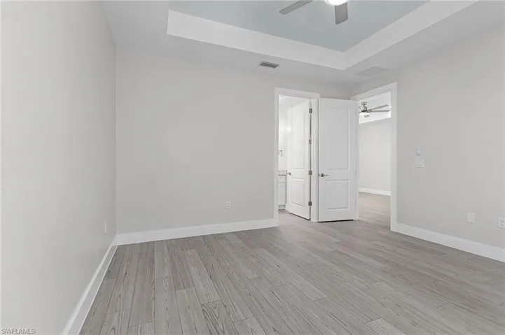 Unfurnished bedroom with a raised ceiling, light wood-style floors, ceiling fan, and ensuite bath