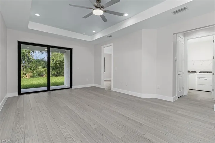 Empty room with washer and dryer, recessed lighting, a raised ceiling, light wood-type flooring, and ceiling fan
