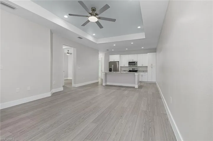Unfurnished living room with ceiling fan, recessed lighting, a tray ceiling, and light wood finished floors