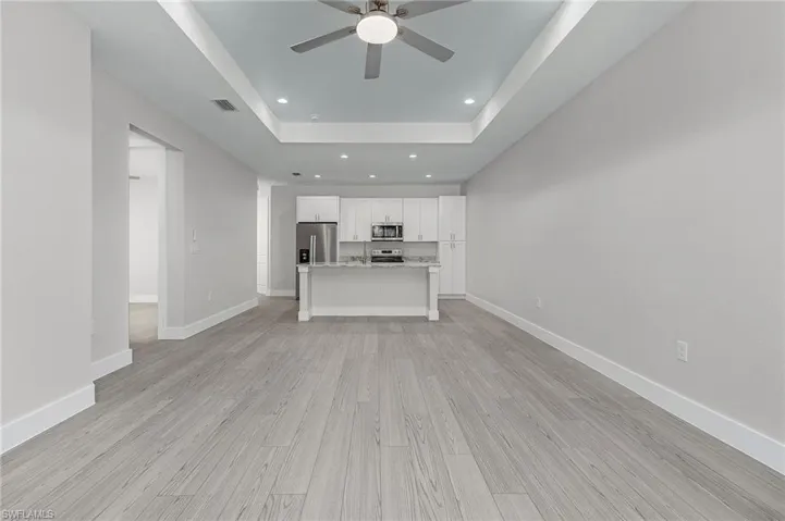 Unfurnished living room with a tray ceiling, recessed lighting, light wood-style floors, and a ceiling fan