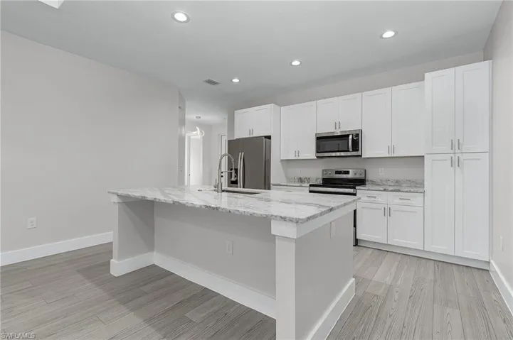 Kitchen featuring light stone countertops, an island with sink, appliances with stainless steel finishes, white cabinetry, and recessed lighting