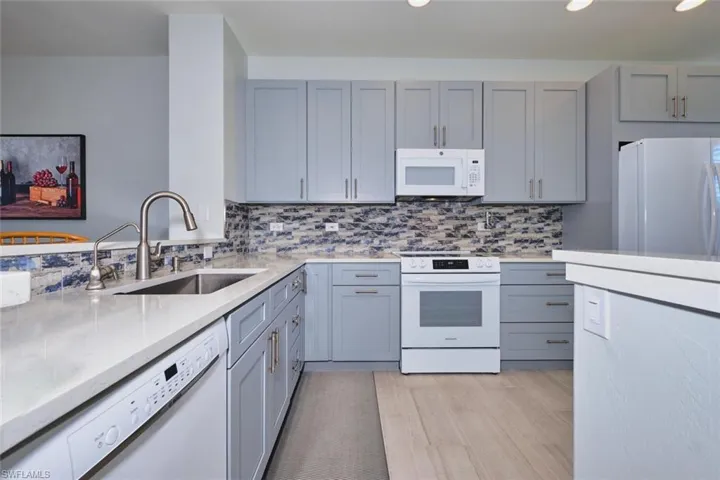 Kitchen featuring gray cabinetry, white appliances, light stone counters, and decorative backsplash