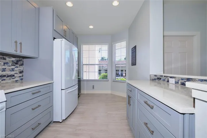Kitchen featuring decorative backsplash, freestanding refrigerator, light stone counters, recessed lighting, and light wood-style flooring