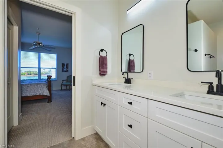 Full bathroom featuring ensuite bath, double vanity, dark carpet, and a ceiling fan