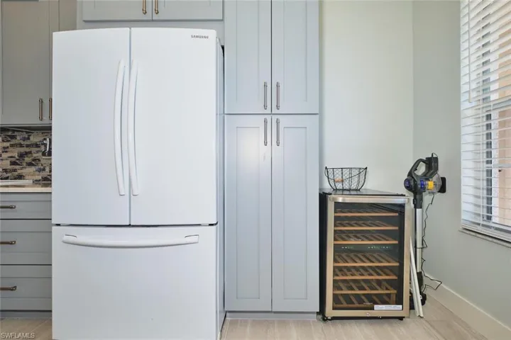 Kitchen featuring freestanding refrigerator, beverage cooler, gray cabinetry, tasteful backsplash, and light wood-style floors