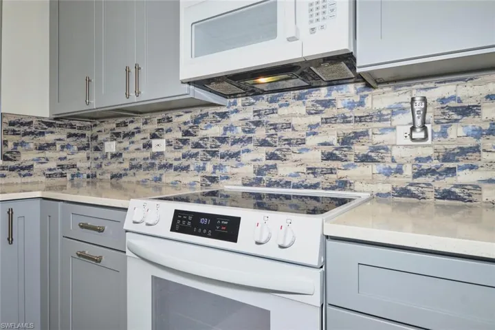 Kitchen featuring white appliances, gray cabinets, light stone countertops, and tasteful backsplash