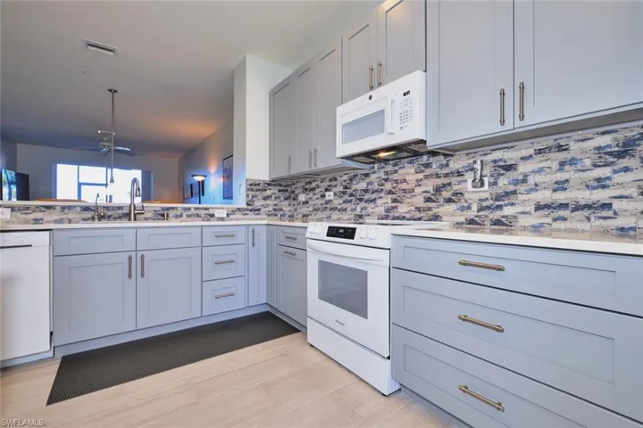 Kitchen featuring white appliances, gray cabinets, a ceiling fan, backsplash, and light stone countertops