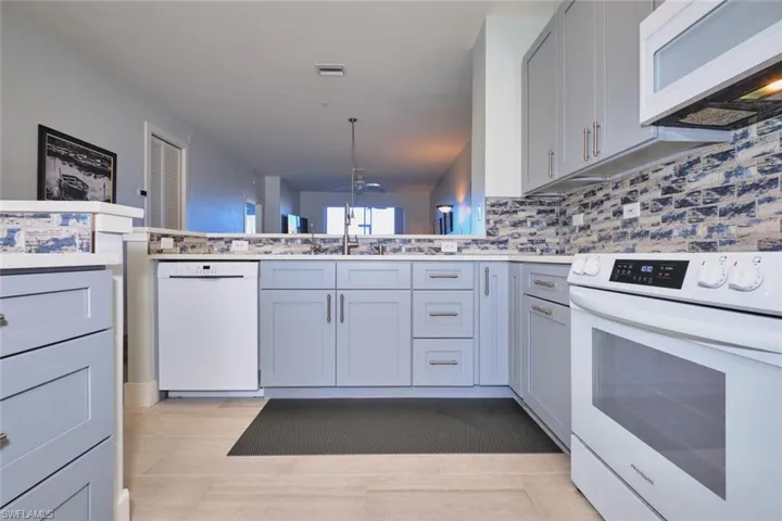 Kitchen featuring white appliances, gray cabinetry, tasteful backsplash, a peninsula, and light stone counters