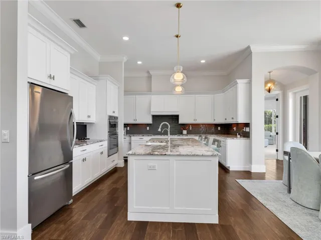Kitchen with arched walkways, light stone counters, stainless steel appliances, a kitchen island with sink, and white cabinetry