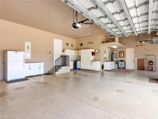 Garage with freestanding refrigerator, water heater, and a garage door opener