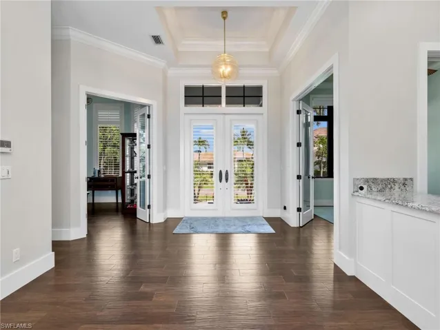 Foyer entrance with french doors, dark wood-style floors, a raised ceiling, and crown molding