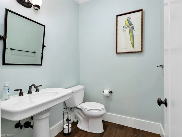 Half bath with dark wood-type flooring and ornamental molding