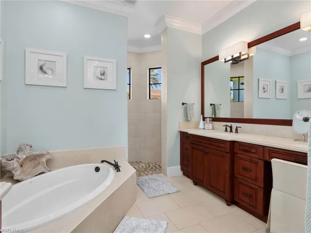 Full bathroom with vanity, a garden tub, a walk in shower, light tile patterned floors, and ornamental molding
