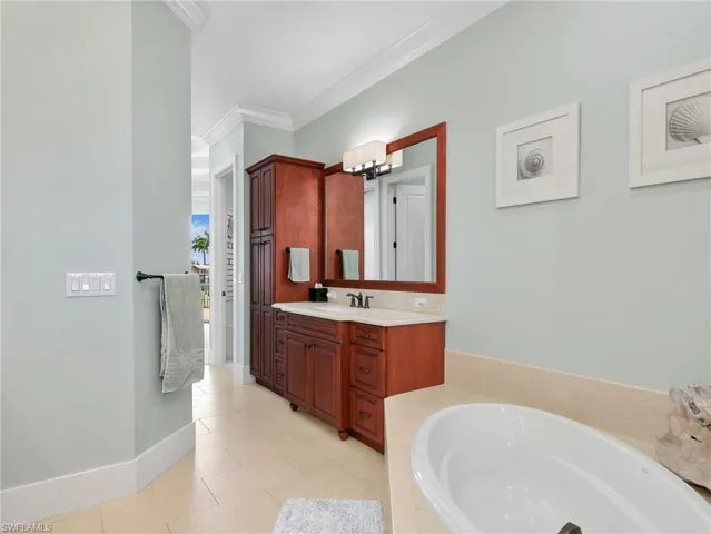 Bathroom with ornamental molding, vanity, a bath, and light tile patterned floors