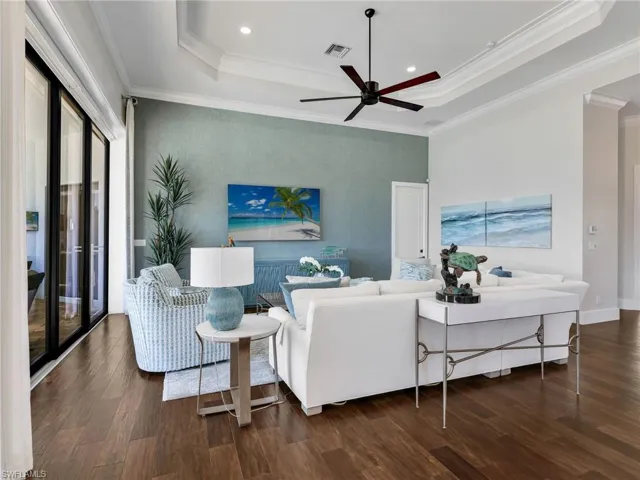 Living area with a ceiling fan, dark wood-style floors, recessed lighting, crown molding, and a raised ceiling
