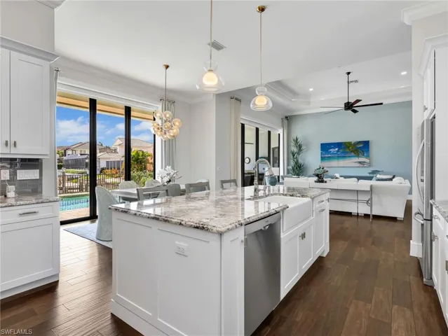 Kitchen featuring white cabinets, an island with sink, ornamental molding, light stone countertops, and dark wood-style floors