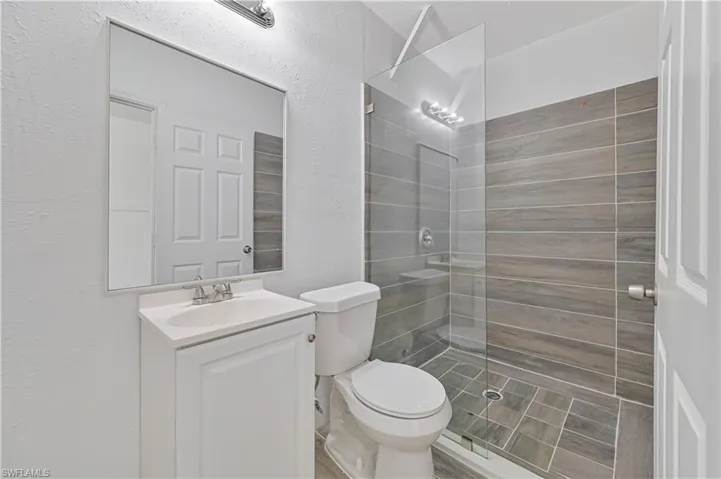Bathroom with a textured wall, tiled shower, and vanity