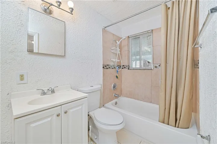 Full bathroom featuring a textured wall, shower / bath combo, a textured ceiling, and vanity