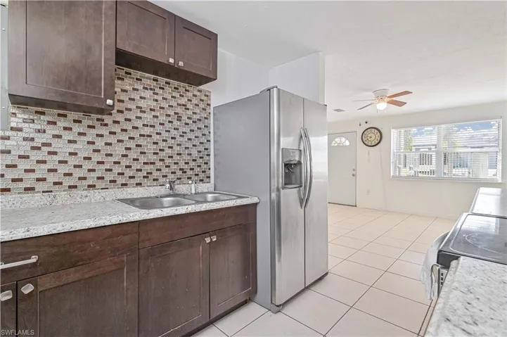 Kitchen with dark brown cabinetry, backsplash, appliances with stainless steel finishes, light tile patterned floors, and a ceiling fan