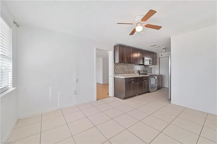 Kitchen with dark brown cabinetry, appliances with stainless steel finishes, light tile patterned floors, tasteful backsplash, and ceiling fan