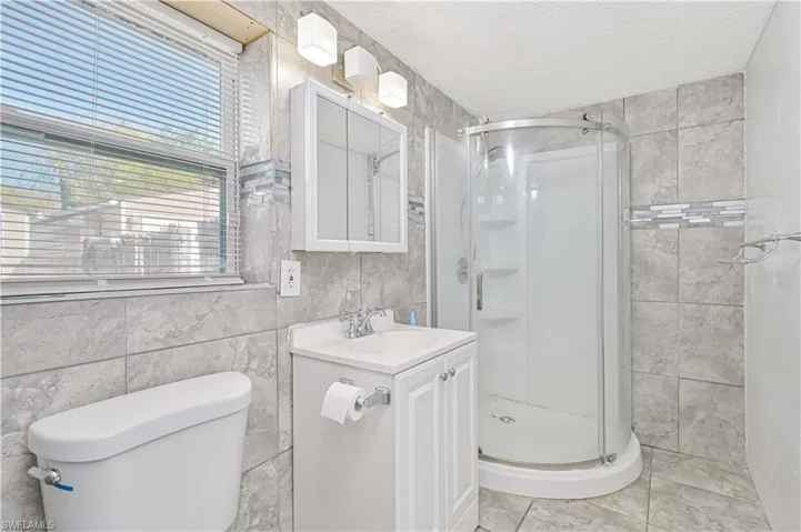 Bathroom with tile walls, a shower stall, a textured ceiling, and vanity