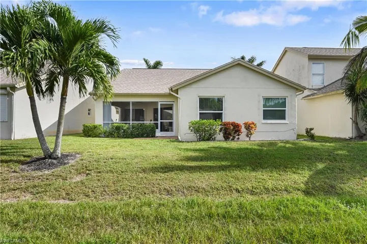 View of back of property featuring a sunroom, stucco siding, a back yard, and a shingled roof