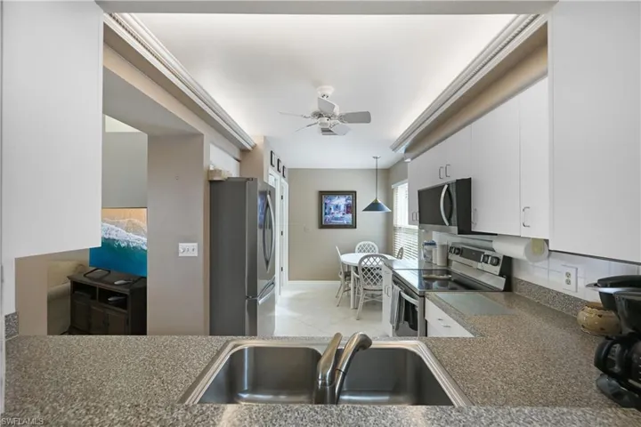 Kitchen featuring stainless steel appliances, white cabinetry, hanging light fixtures, a ceiling fan, and dark countertops