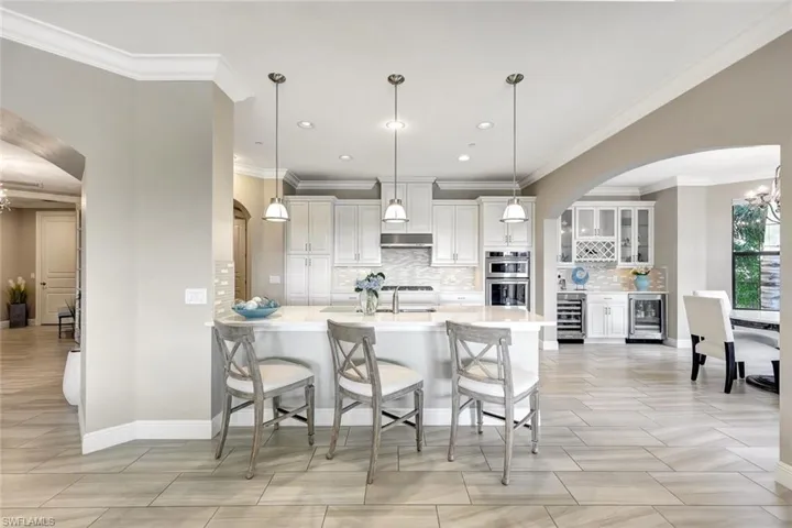 Kitchen featuring double oven, ornamental molding, hanging light fixtures, and beverage cooler