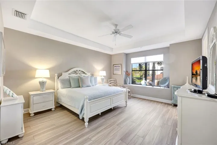 Bedroom with light wood-type flooring, a tray ceiling, and ceiling fan