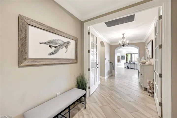 Hall with light hardwood /wood-style floors, ornamental molding, and an inviting chandelier