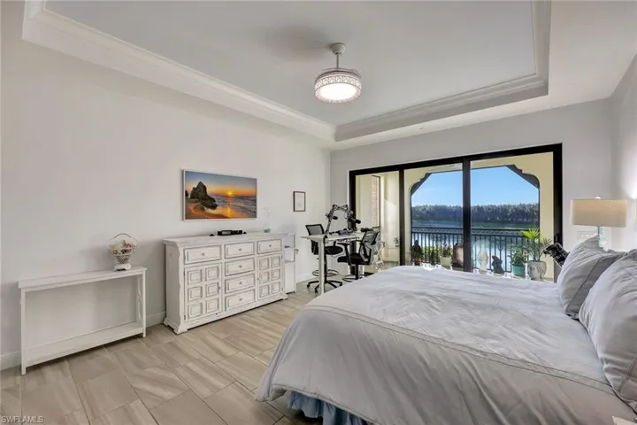 Bedroom with a tray ceiling, access to exterior, a water view, and ornamental molding