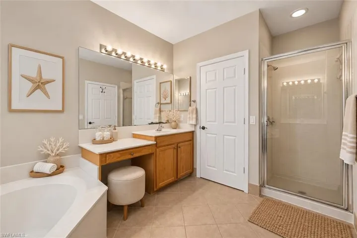 Tiled flooring, built-in vanity with wood cabinetry, large vanity mirror, glass-enclosed shower, and a built-in corner bathtub