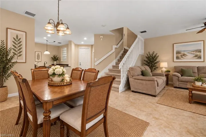 Spacious dining area with chandelier lighting, wood-finish flooring, and a staircase featuring white railings