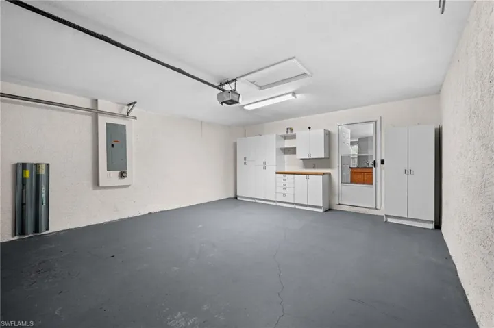 Integrated garage with epoxy-coated flooring, built-in white cabinetry, and wood-finish countertops