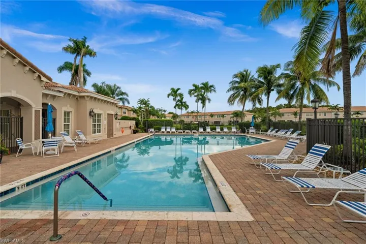 Spacious swimming pool with brick paver decking, adjacent clubhouse structure, and mature palm landscaping