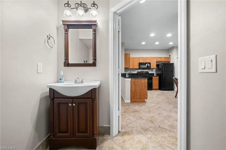 Ceramic tile flooring, wood-finish vanity with integrated basin, three-light vanity fixture, black appliances, wood-finish cabinetry